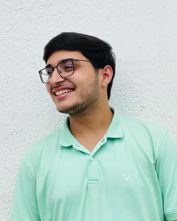 Vaibhav Dhand smiling and looking to the side, wearing glasses and a mint green polo shirt, in front of a white wall.